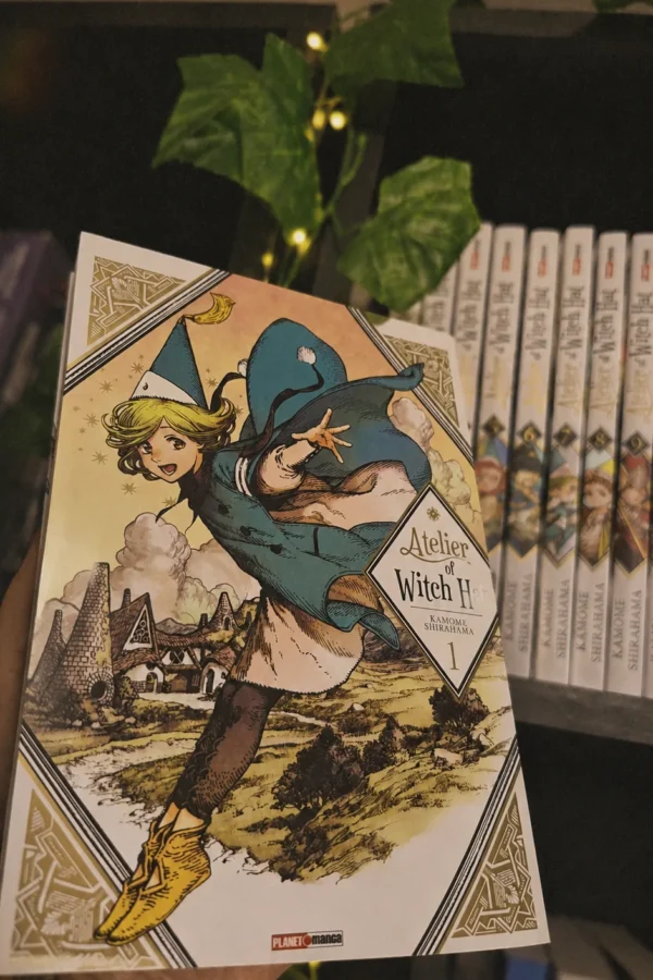 o volume 1 de witch hat atelier, de kamome shirahama, segurado na mão diante da estante
